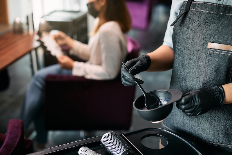 Close-up of hairdresser preparing dye in a container at hair salon.
