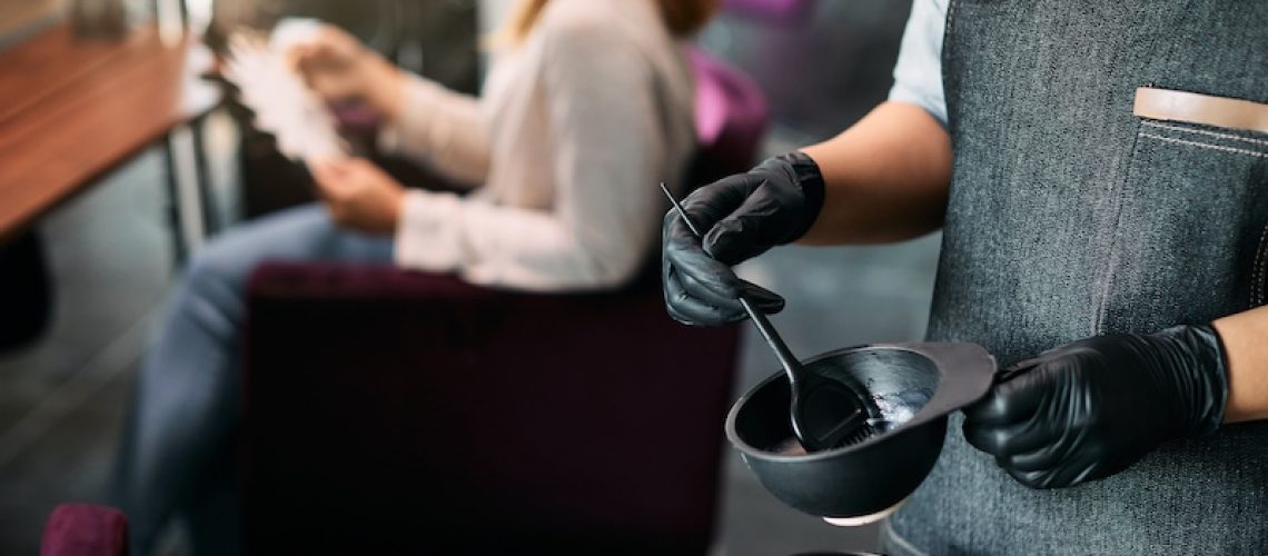 Close-up of hairdresser preparing dye in a container at hair salon.